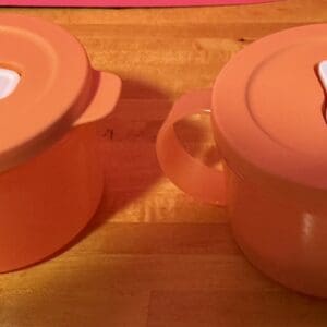 Two orange ceramic kitchen pots with lids on a wooden surface.