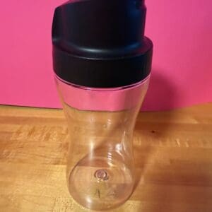 Clear water bottle with black lid and pink grip on wooden table.