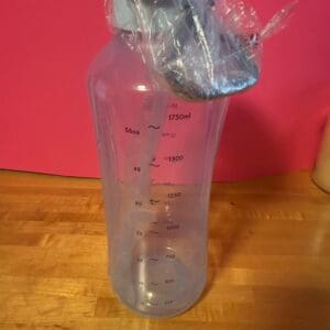 Clear plastic measuring bottle with a spout on a wooden surface.