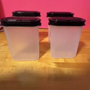 Four translucent plastic containers with black lids on a wooden surface.