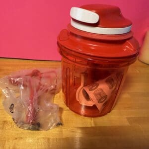 Red container with a white lid and a small plastic bag on a wooden surface.