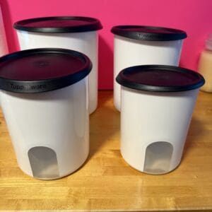 White plastic kitchen containers with black lids on a wooden surface.