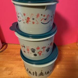 Stacked Christmas-themed plastic containers with festive designs on a pink background.