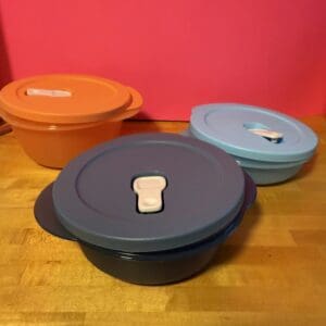 Three colorful Tupperware containers with lids on a wooden table.