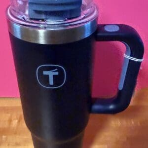 Black insulated travel mug with a handle and clear lid on wooden surface.