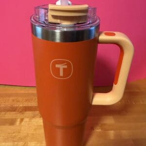 Orange travel mug with beige handle and cork lid on wooden surface.