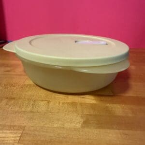 Plastic container with lid on wooden surface against pink background.