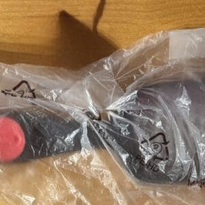 A packaged black frying pan with a red button handle on a wooden surface.