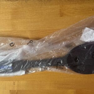 A black metal car part wrapped in plastic on a wooden floor.