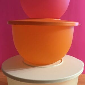Stacked colorful plastic bowls with lids against a pink background.