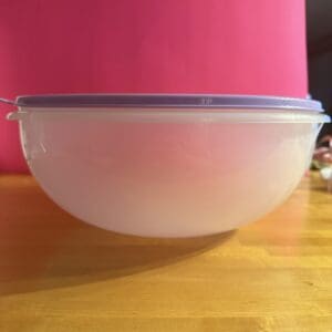 A transparent bowl with a white lid on a wooden surface.