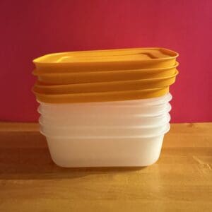 Stacked plastic containers with yellow lids on a wooden surface.