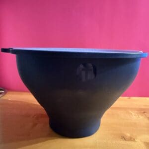 Black ceramic bowl on a wooden surface with a pink background.
