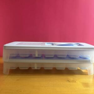 Two transparent plastic ice cube trays stacked on a wooden surface.