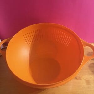 Bright orange plastic bowl with handles on a wooden surface.