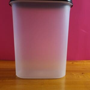 A translucent plastic container on a wooden surface with a pink background.
