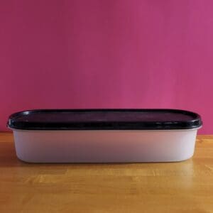 Rectangular white container with a black lid on a wooden surface.