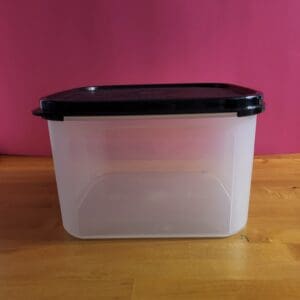 A clear plastic container with a black lid on a wooden surface.