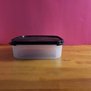 A black-lidded plastic container on a wooden surface with a pink background.