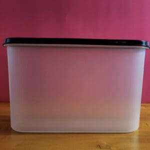 Rectangular translucent plastic container with a black lid on a wooden surface.