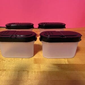 Four white plastic containers with black lids on a wooden surface.