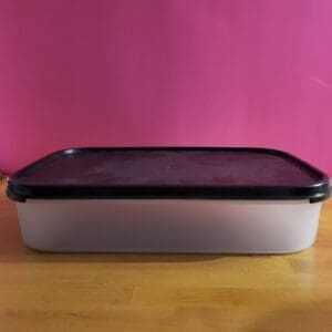 Rectangular metal container with a black lid on a wooden surface.