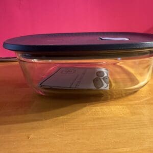 Glass food storage container with black lid on wooden surface.